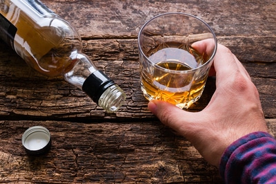 Talke with bottle turned on its side and a person with a glass of amber liquid.