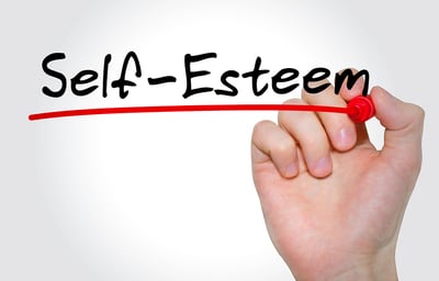 Person writing the word self-esteem in black with a red link underneath.