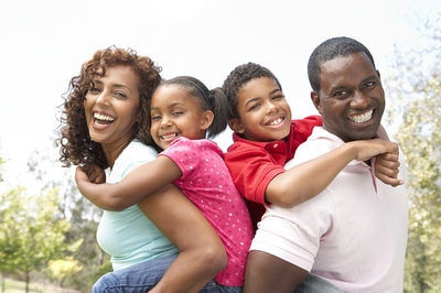 African American family smiling with trees in the background.