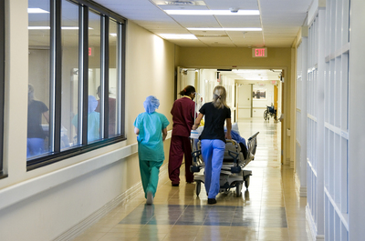 Person being pushed in a hospital bed down a hallway.