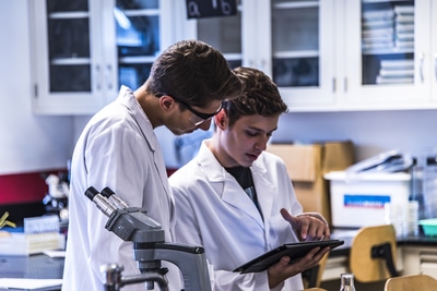 Two scientists with white lap coats looking at a tablet together.
