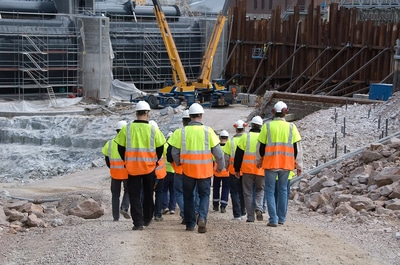 Group of workers with reflective vests and hard hat entering a construction site.