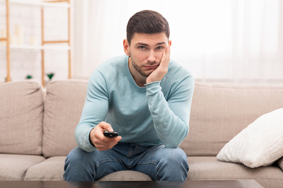 Man sitting on a couch using a tv clicker.