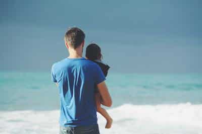 Father carrying a child on the beach.