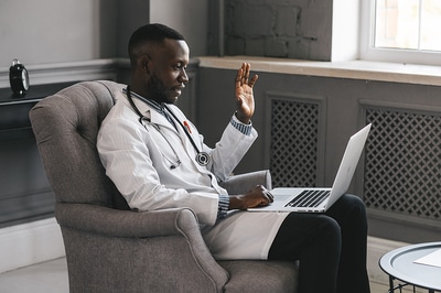 Medical doctor sitting in a chair using his laptop for a Telehealth visit.